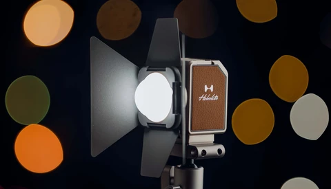 Professional LED light with reflector and brown leather case displayed against blurred bokeh background.
