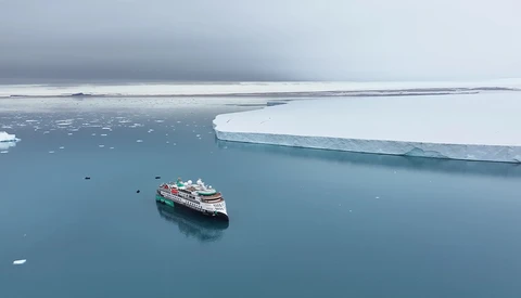 Expedition cruise ship navigating through icy Arctic waters surrounded by white ice floes and a massive ice shelf.