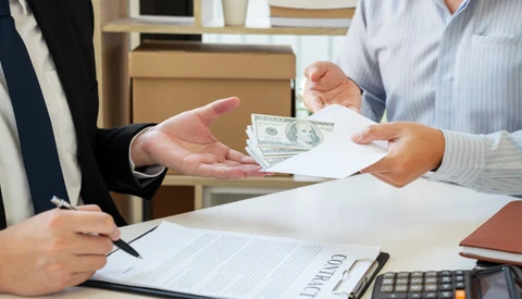 Two people exchange cash and documents at a desk during a business transaction.