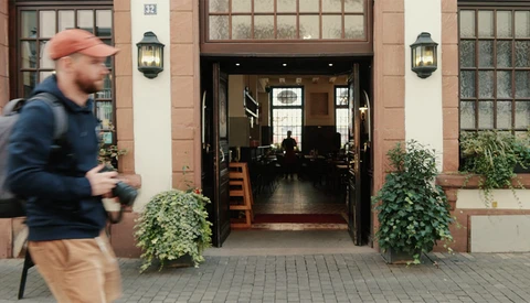 Man in orange cap and blue jacket jogging past a brownstone storefront with arched entrance.