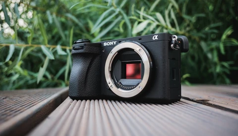 Sony Alpha mirrorless camera body displayed on wooden surface with blurred foliage background.