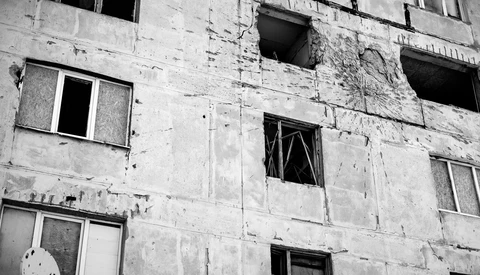 Abandoned concrete apartment building with boarded windows and crumbling facade.
