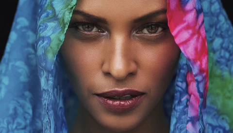 Close-up portrait of a woman wearing colorful blue and pink patterned fabric draped around her head.