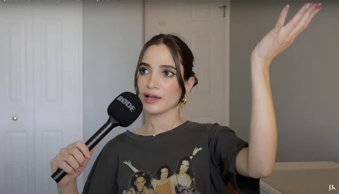 Woman holding microphone during an indoor interview or presentation, gesturing with raised hand.