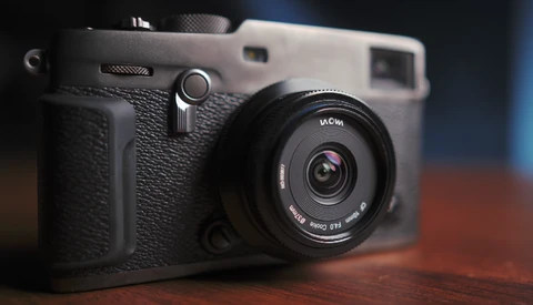 Instant film camera with black textured body and fixed lens on wooden surface.