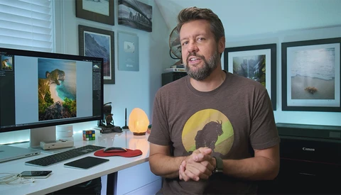 Photographer in a studio speaking toward camera while wearing a graphic t-shirt.