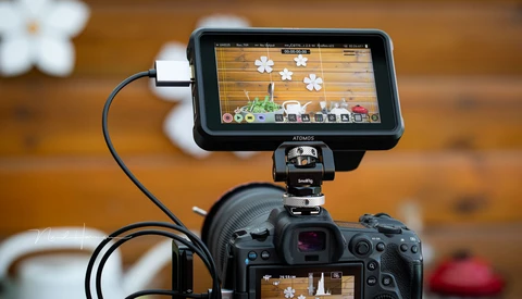 External monitor mounted on camera showing live video feed with editing interface and flower graphics.