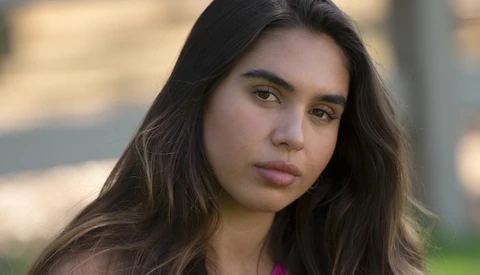 Young woman with long dark hair looking directly at camera with neutral expression.