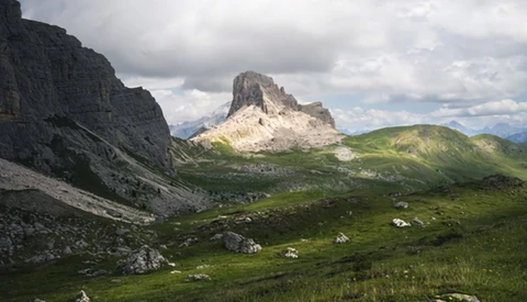 Alpine valley with steep rocky peaks and lush green meadows under cloudy sky.