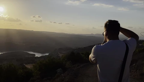 Photographer silhouetted against a vast landscape with mountains and a winding river at golden hour.
