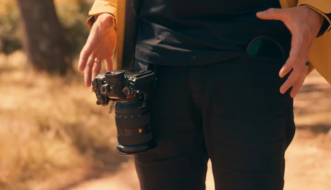Photographer holding a mirrorless camera with telephoto lens during golden hour outdoor shoot.