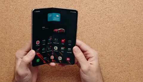 Hands holding a foldable smartphone with dark interface displaying app icons and a red car image.