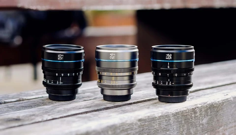 Three vintage cinema lenses arranged in a row on a wooden surface, displaying blue, silver, and blue lens barrels with manual focus rings.