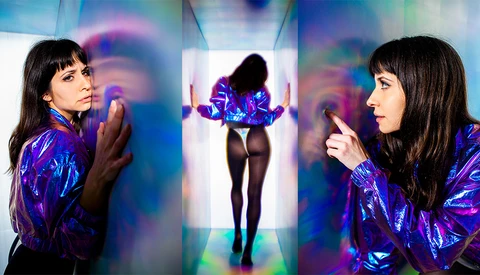 Woman in iridescent purple jacket posed against colorful light streaks and geometric reflections.