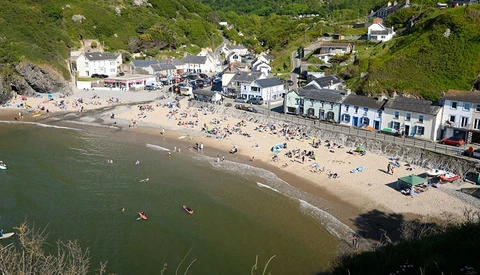 Aerial view of a crowded beach cove with seaside buildings and boats in shallow water.