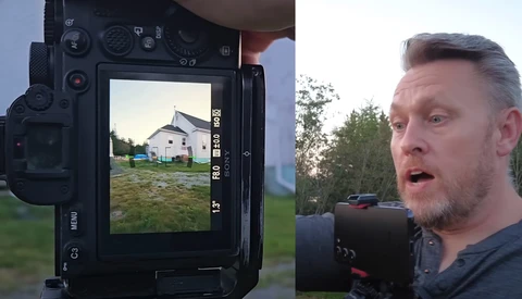 Photographer holding cinema camera while monitoring a residential property on the camera's rear display screen.