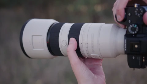 Photographer holding a white telephoto lens attached to a camera body with visible focus ring and depth-of-field markings.