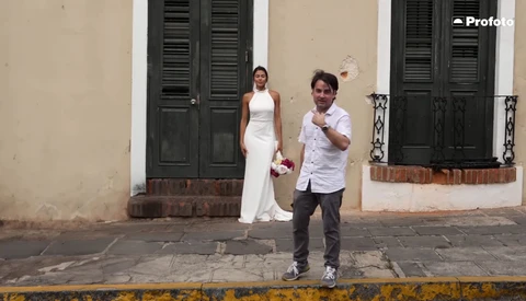Couple walking together on a colonial-style street with cream and black shuttered buildings.