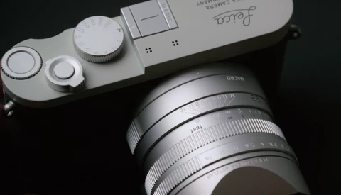 Silver mirrorless camera body with attached lens and visible control dials, photographed against a black background.