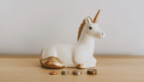 White ceramic unicorn figurine with gold accents and four small gold coins arranged in front.