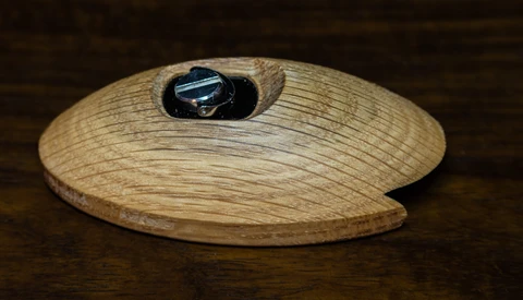 Wooden oval dish with grain texture and a dark metal ring recessed into its surface.