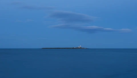 Cargo ship on the horizon under a blue sky with wispy clouds and calm sea.