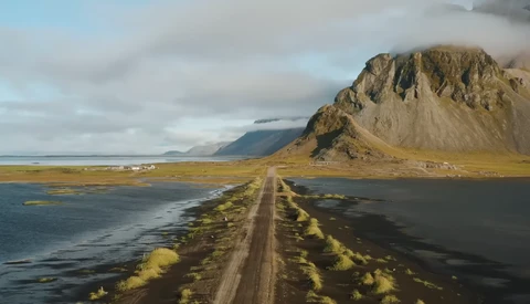 Gravel road stretching toward a distinctive peaked mountain across black sand plains with moss-covered terrain.