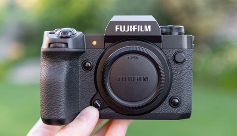 Fujifilm X-H2S mirrorless camera body held in hand against blurred green background.
