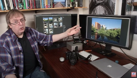 Photographer at desk with dual monitors showing photo editing software and a camera.