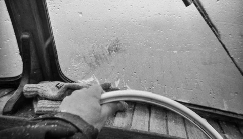 Black and white photograph of a hand holding a car door handle with rain droplets covering the vehicle's surface.
