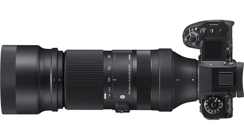 Mirrorless camera with telephoto lens attached, shown in profile against white background.
