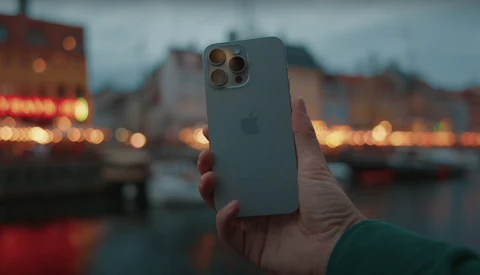 Hand holding iPhone 12 Pro with triple camera setup against blurred evening cityscape with warm lights.
