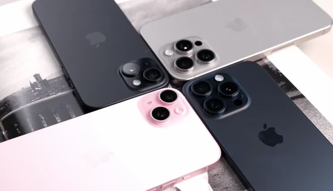 Four iPhones arranged on a white surface, displaying various color options including black, silver, pink, and midnight blue with triple-lens camera systems.