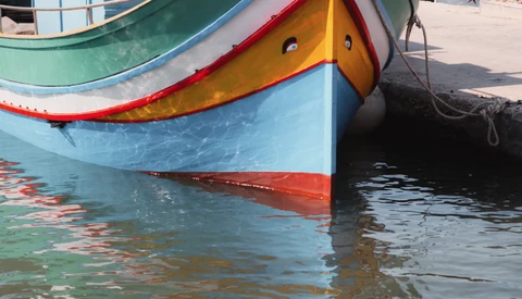 Colorful fishing boats with blue, yellow, and red hulls moored in shallow turquoise water.