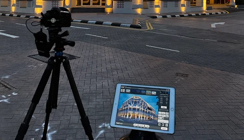 Professional camera on tripod pointed at tablet displaying architectural photograph on urban street at dusk.