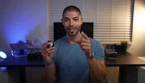 Man in blue t-shirt holding a camera in a home studio setting with blue and warm lighting.