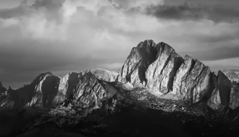 Dramatic black and white mountain landscape with jagged peaks and stormy sky overhead.