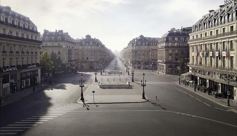 Wide boulevard lined with Haussmann-style buildings, wet pavement reflecting overcast sky, architectural symmetry receding to vanishing point.