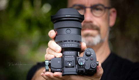 Photographer holding Sony mirrorless camera with telephoto lens, displayed toward camera.