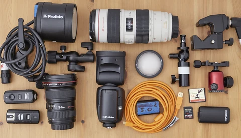 Professional photography equipment laid out flat on wooden surface including lighting, lenses, cables, and accessories.