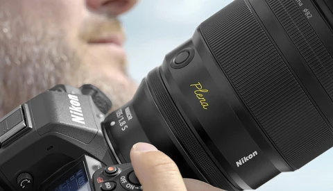 Photographer holding a Nikon camera with a prime lens featuring a gold nameplate marking.