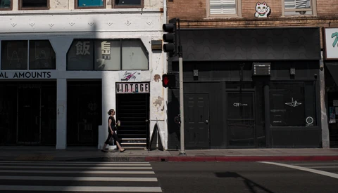 Person walking across crosswalk in front of storefronts with mixed architectural styles and signage.