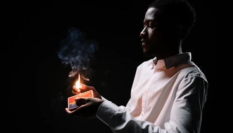 Person holding a lit candle against a dark background, with smoke rising from the flame.