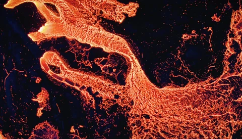 Aerial thermal or infrared view of flowing lava with bright orange and yellow channels against dark cooled rock.
