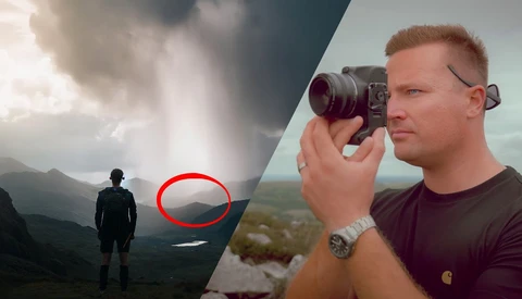 Photographer holding a camera on a mountainside as another figure stands in a distant valley below dramatic cloudy skies.