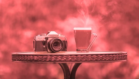 Vintage rangefinder camera and glass of red juice on decorative table against pink bokeh background.