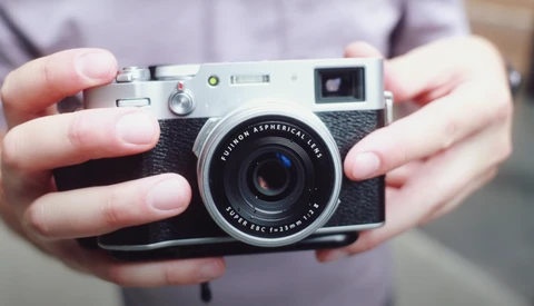 Hands holding a rangefinder camera with Fujinon Aspherical lens against a purple shirt.