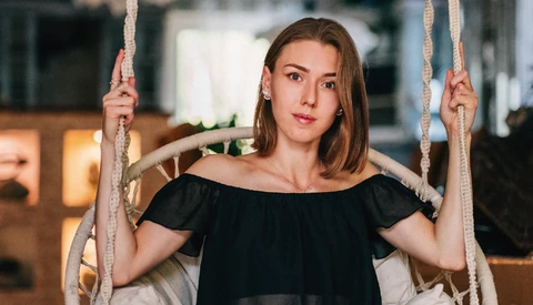 Young woman in black off-shoulder top holding rope swing ropes while looking at camera.
