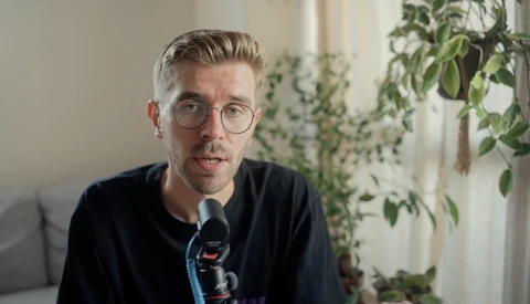 Man wearing glasses and dark shirt speaking into microphone during interview or podcast recording.