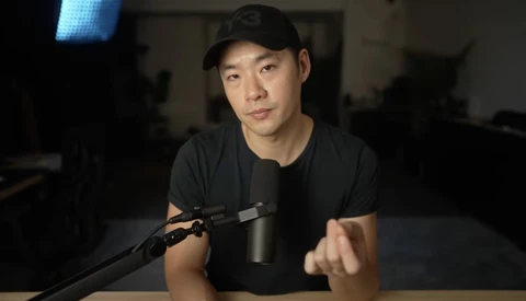 Person speaking into a microphone in a dimly lit studio setting.